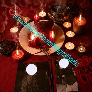 Può includere: Un allestimento rituale su una superficie rossa con un piatto bianco centrale contenente un oggetto scuro a forma di cuore, circondato da diverse candele rosse e bianche accese, fumo d'incenso, un bruciatore in metallo e due foto in bianco e nero.