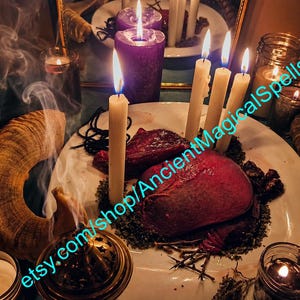 Puede incluir: Un plato blanco contiene dos objetos de color rojo oscuro en forma de corazón rodeados de hierbas secas y ramitas. Cuatro velas altas encendidas de color crema y una vela morada grande están presentes, junto a un cuerno, un incensario y frascos.