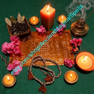 Pode incluir: Uma folha retangular de cor dourada com símbolos gravados, rodeada por quatro velas acesas, uma tigela de madeira com grãos de pimenta preta e folhas de louro, um incensário de latão com fumo, flores cor-de-rosa e um colar de contas.