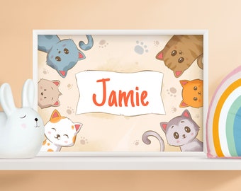 May include: A white framed print with a beige background featuring a cartoon illustration of six cats with different coloured fur. The cats are arranged in a circle around a white banner with the name "Jamie" written in orange text.