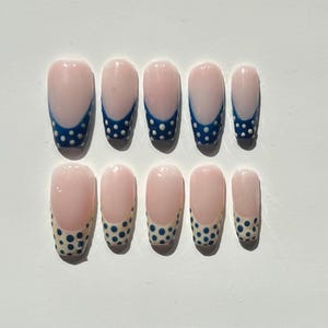 May include: A set of ten artificial nails. Each nail is a light pink color with a white tip and a blue dotted design. The nails are arranged in two rows of five.