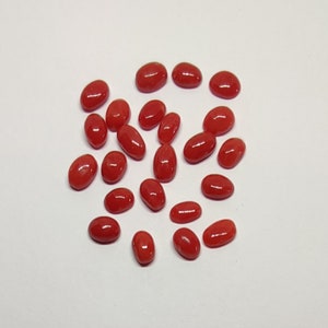 Könnte beinhalten: Eine Ansammlung oval geformter, polierter roter Edelsteine, die auf einer weißen Oberfläche verstreut sind. Die Edelsteine haben eine glatte, glänzende Oberfläche und variieren leicht in Größe und Form. Die leuchtend rote Farbe ist durchgängig.
