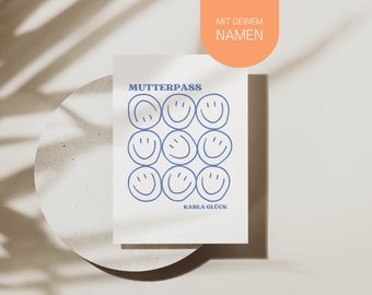 May include: A white card with the text "MUTTERPASS" in blue letters. The card has a grid of nine blue smiley faces. The text "KARLA GLÜCK" is at the bottom of the card. The card is on a light brown surface with a shadow.