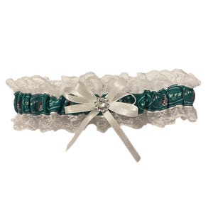 May include: White lace garter with a green ribbon featuring the New York Jets logo and a white bow with a rhinestone embellishment.