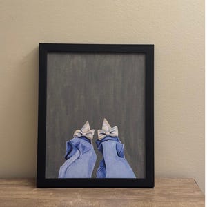 May include: DIY Bedazzle Kit with a 20 x 25 cm canvas. The kit includes a hand-painted canvas, rhinestones, glue, tweezers, and a white pick. The artwork features two figures in blue robes with bows. The canvas is in a black frame.
