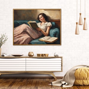 May include: A painting of a woman in a pink dress reading a book while reclining on a blue couch. The woman has dark hair and is wearing a white blouse. The painting is framed in gold.