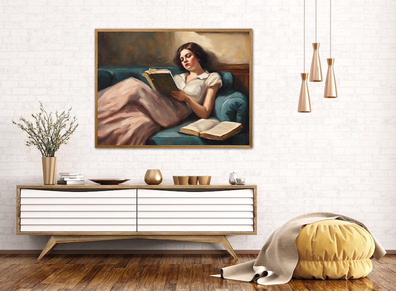 May include: A painting of a woman in a pink dress reading a book while reclining on a blue couch. The woman has dark hair and is wearing a white blouse. The painting is framed in gold.