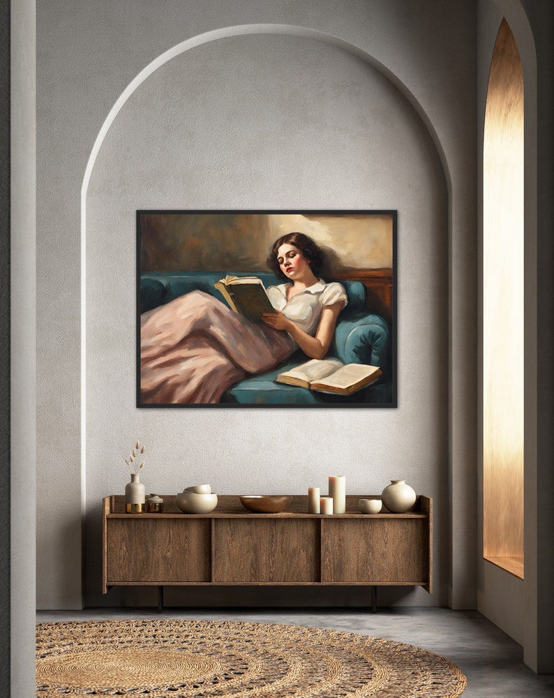 May include: A woman in a white shirt and pink skirt is sitting on a blue couch and reading a book. The couch is in a room with a brown wooden cabinet and a rug.