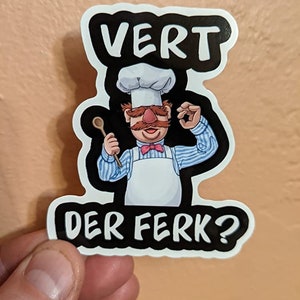 May include: A black and white sticker with a cartoon chef wearing a white chef's hat and a blue and white striped shirt. The chef is holding a wooden spoon in one hand and making a 'OK' sign with the other. The text "VERT DER FERK?" is written in white letters on a black background.