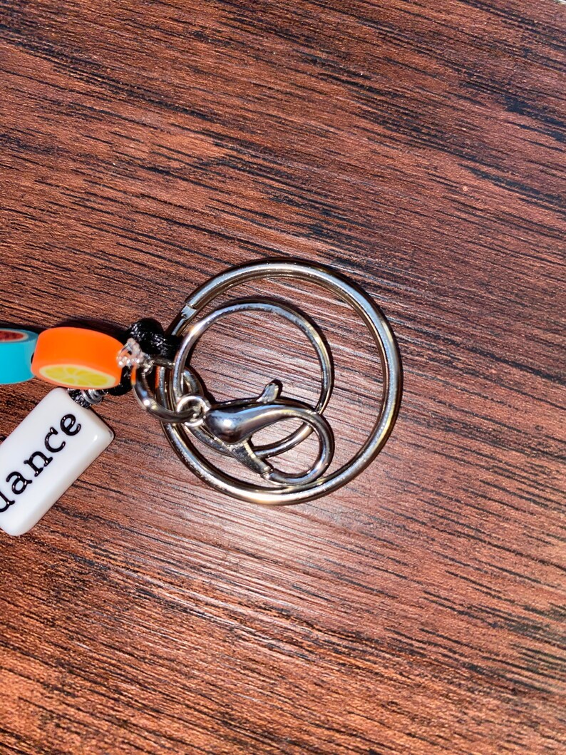 May include: A silver key ring with a small white tag that says "dance" and a colourful charm with orange, blue, and white beads.
