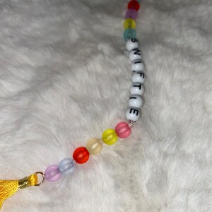 May include: A colourful beaded keychain with a tassel. The beads spell out the word "SWIFTIE".