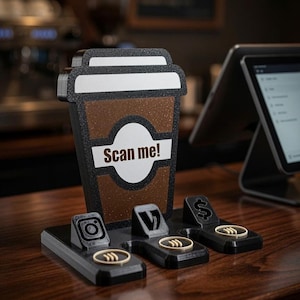 May include: A black and brown coffee cup-shaped sign with the text Scan me! in white. The base features three black triangular stands with social media and payment icons, including an Instagram logo, a Venmo logo, and a dollar sign symbol.