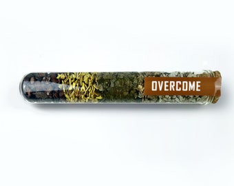 May include: A glass test tube filled with various dried herbs and spices, labeled "OVERCOME".