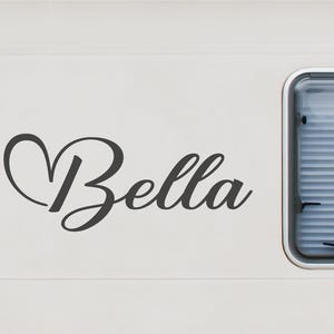 Könnte beinhalten: Ein dunkelgrauer Vinyl-Aufkleber mit dem Namen Bella in einer geschwungenen Schreibschrift, bei dem die erste Buchstabe in eine Herzform integriert ist. Das Bild zeigt zudem drei kleinere kreisförmige Beispiele mit den Namen Molly, Oskar und Runner.