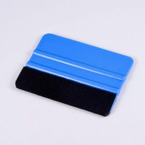 Könnte beinhalten: Ein blauer Kunststoffschieber mit einem schwarzen Filzrand. Der Schieber hat zwei erhabene Linien auf der Oberfläche.