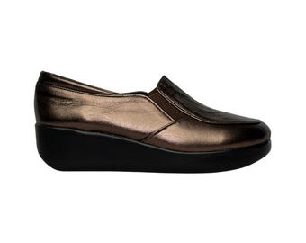 May include: A pair of brown leather slip-on shoes with a wedge heel. The shoes have a metallic finish and a black rubber sole.