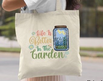 May include: A natural canvas tote bag with the text "Life is Better in the Garden" and a graphic of a mason jar with fireflies and plants inside.