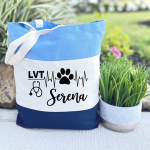 May include: A blue and white canvas tote bag with a stethoscope, heartbeat, paw print, and the text "LVT Serena".