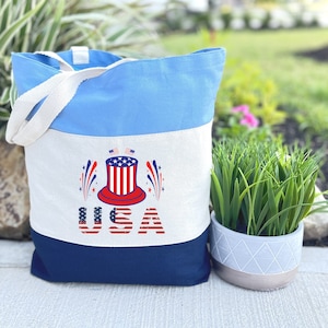 May include: A blue, white, and navy blue canvas tote bag with a red, white, and blue patriotic design. The design features a top hat with stars and stripes, fireworks, and the word "USA".