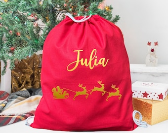 May include: Red Christmas gift bag with a gold drawstring and the name "Julia" printed on the front. The bag features a gold silhouette of Santa Claus in his sleigh pulled by reindeer.