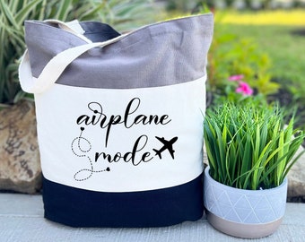May include: A tri-color tote bag with a gray, white, and black design. The bag has a white panel with the text "airplane mode" and a small airplane graphic.