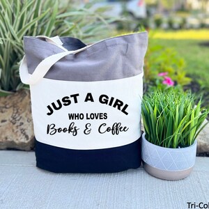Puede incluir: Una bolsa de tela gris de tres colores con un panel blanco que dice "Just a girl who loves books & coffee".