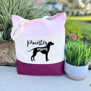 May include: A tri-color tote bag with a pink, white, and burgundy design. The bag features a black silhouette of a pointer dog with the text "Pointer Mom" printed on the white section.