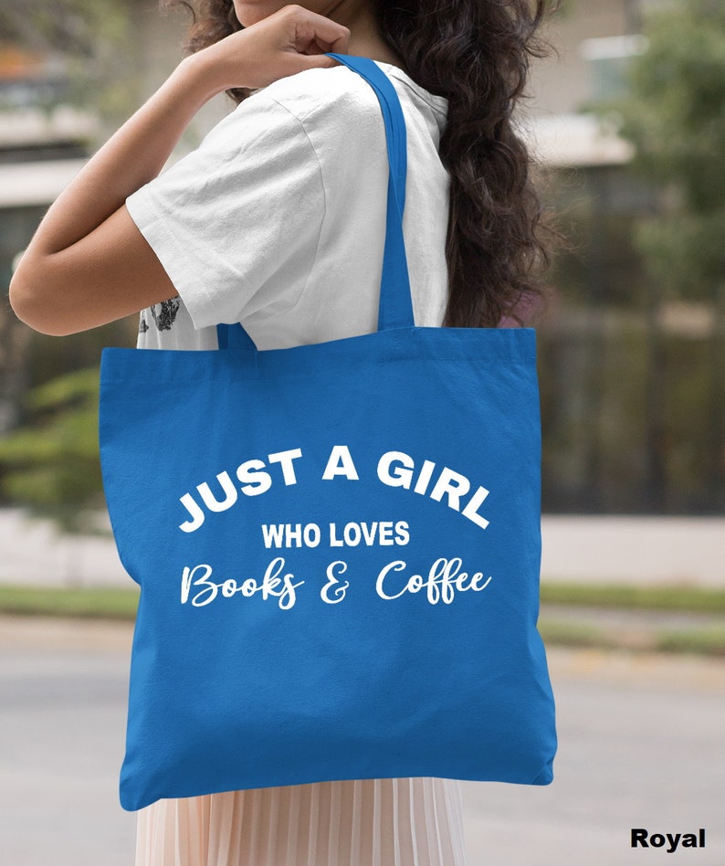 Puede incluir: Una bolsa de tela azul real con texto blanco que dice "Just a girl who loves books & coffee".
