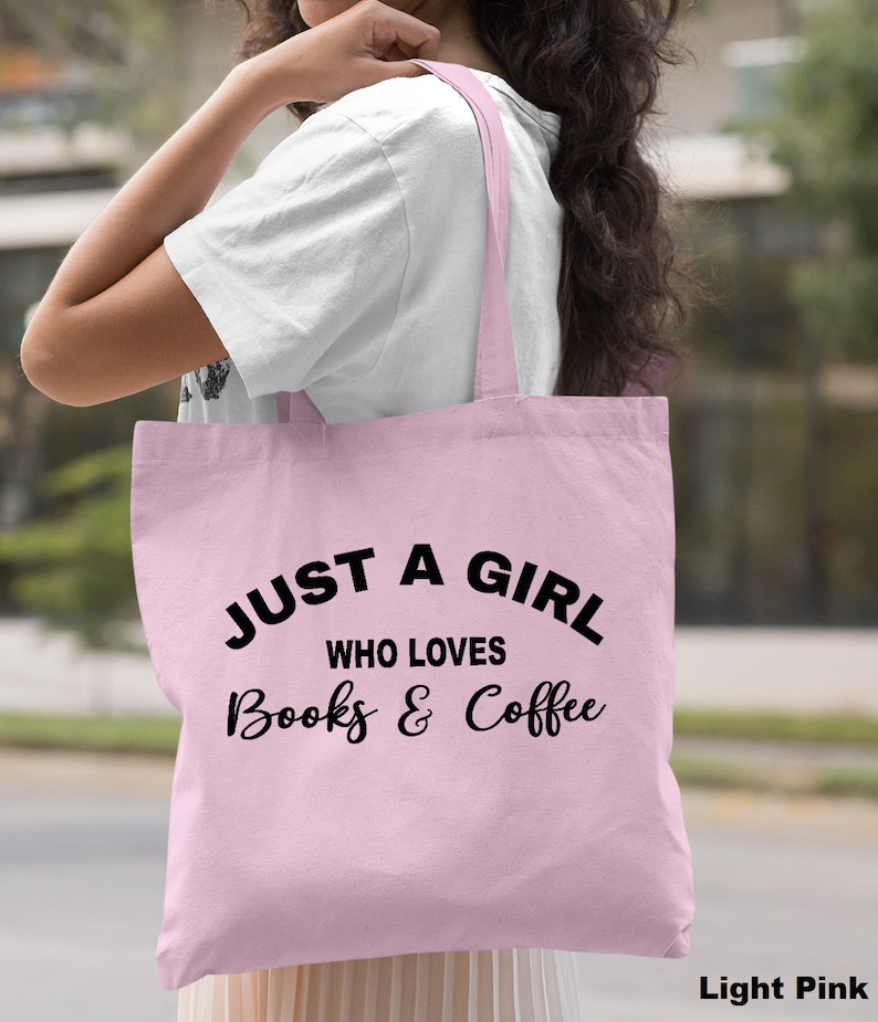 Puede incluir: Una bolsa de tela de color rosa claro con el texto "Just a girl who loves books & coffee" en negro.