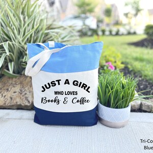 Puede incluir: Una bolsa de tela de color tricolor con tejido azul, blanco y azul marino. La bolsa tiene dos asas blancas y el texto "Just a girl who loves books & coffee" impreso en la secci&oacute;n de tela blanca.