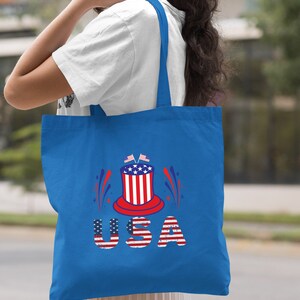 May include: A royal blue tote bag with a red, white, and blue USA graphic. The graphic features a top hat with stars and stripes, fireworks, and the word "USA" in red, white, and blue letters.