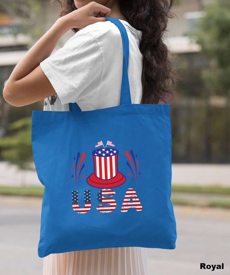 May include: A royal blue tote bag with a red, white, and blue USA graphic. The graphic features a top hat with stars and stripes, fireworks, and the word "USA" in red, white, and blue letters.