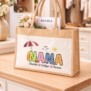 May include: A beige tote bag with a white pocket featuring the word "NANA" in colorful letters, a beach umbrella, and the names Charles, Evelyn, and Aaron. The bag contains a magazine and flowers.
