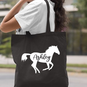 May include: Black canvas tote bag with a white silhouette of a horse and the name "Ashley" printed on it.