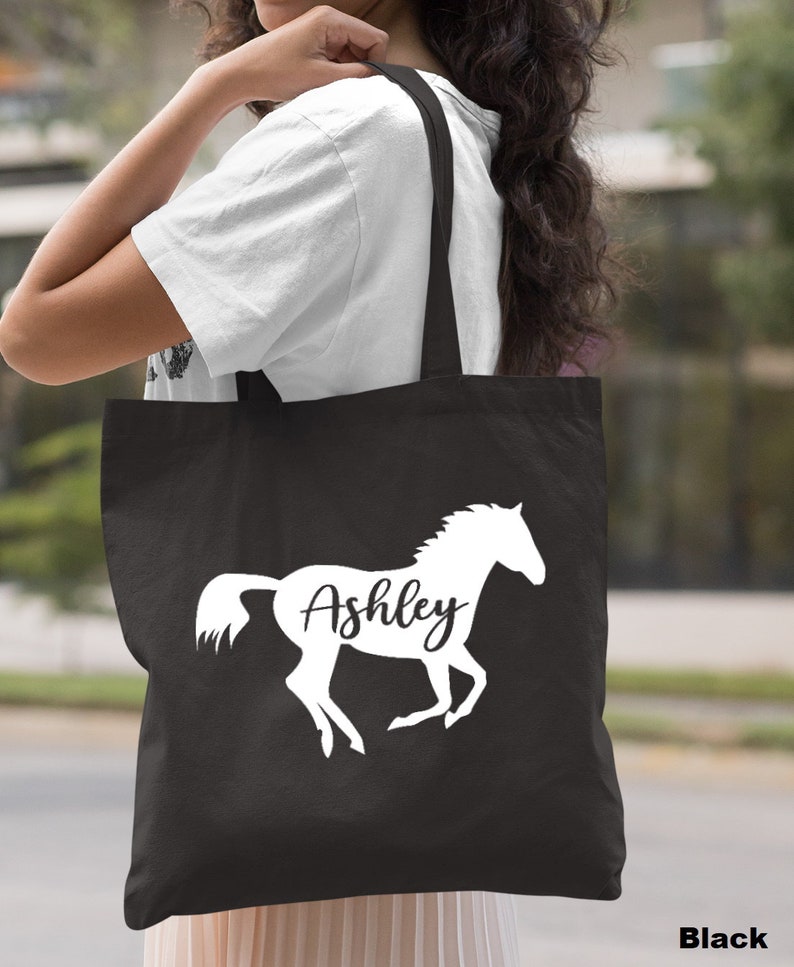 May include: Black canvas tote bag with a white silhouette of a horse and the name "Ashley" printed on it.