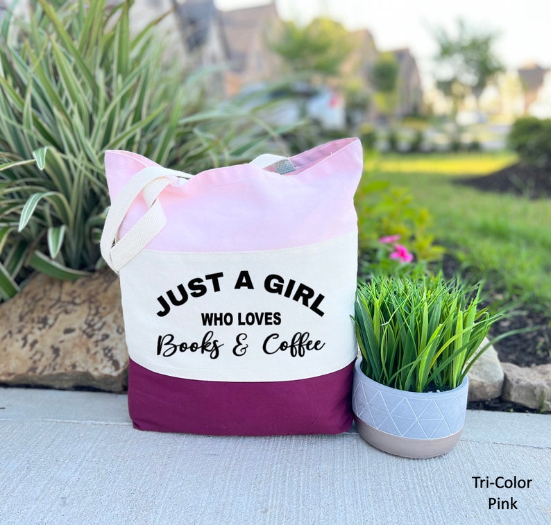 Puede incluir: Una bolsa de mano tricolor con un dise&ntilde;o rosa, blanco y burdeos. La bolsa tiene un panel de lona blanco con el texto "Just a girl who loves books & coffee".