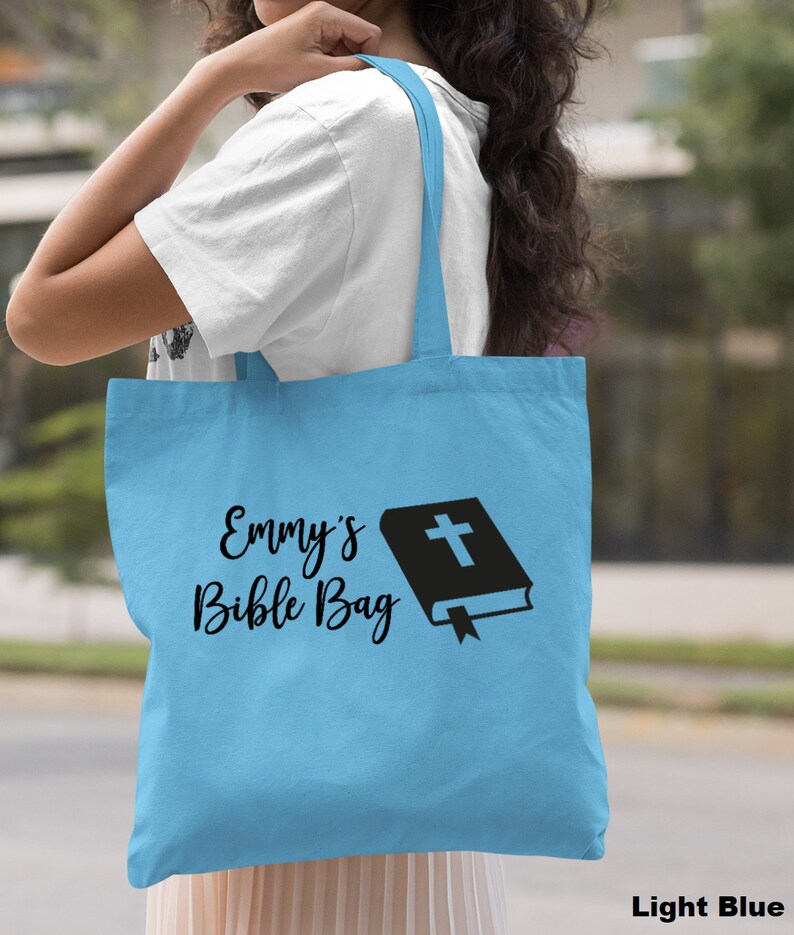 May include: Light blue tote bag with the text "Emmy's Bible Bag" and a black silhouette of a closed book with a cross on the cover.