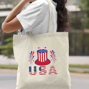 May include: A natural canvas tote bag with a red, white, and blue graphic of a top hat with fireworks and the word "USA" in red, white, and blue.