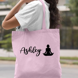 Pu&ograve; includere: Borsa tote rosa chiaro con il nome "Ashley" e la silhouette di una persona in una posa yoga.