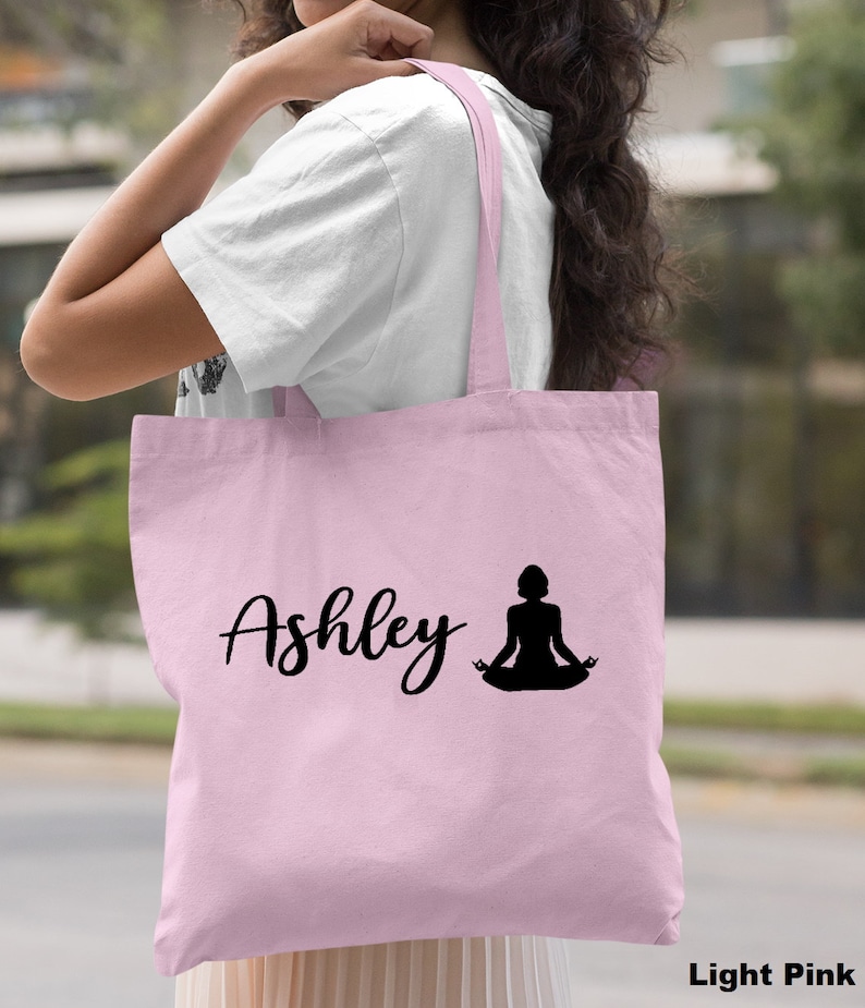 Pu&ograve; includere: Borsa tote rosa chiaro con il nome "Ashley" e la silhouette di una persona in una posa yoga.