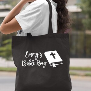 May include: Black canvas tote bag with white text that says "Emmy's Bible Bag" and a white image of a closed book with a cross on the cover.