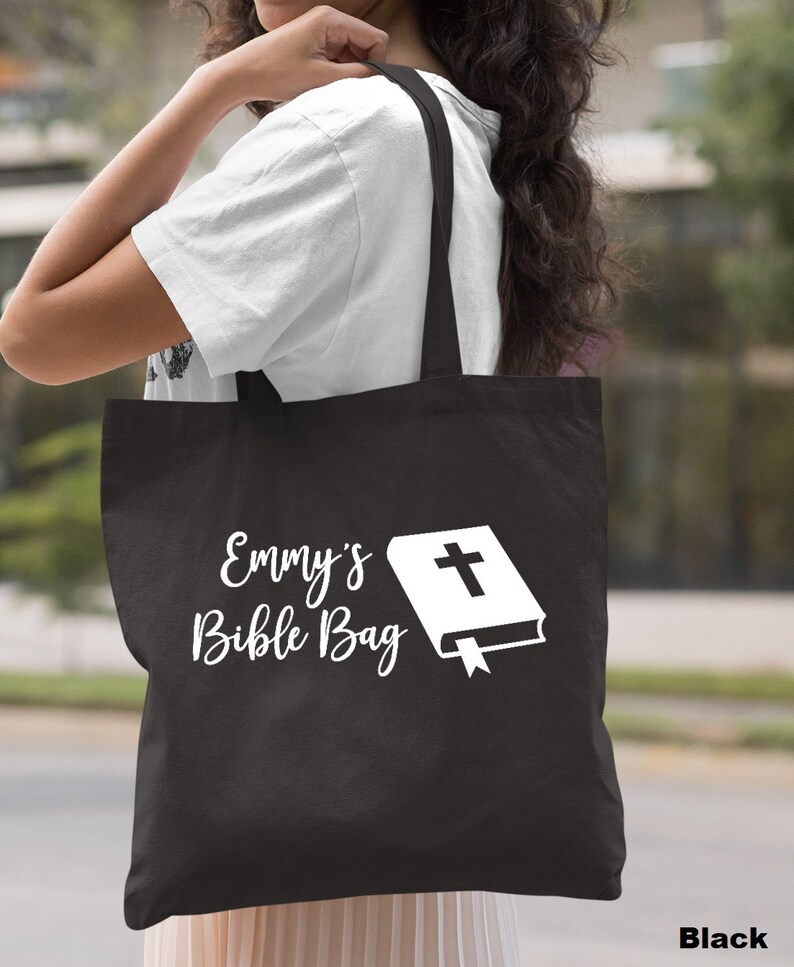 May include: Black canvas tote bag with white text that says "Emmy's Bible Bag" and a white image of a closed book with a cross on the cover.