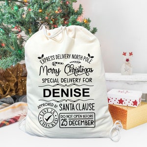 May include: A white canvas Christmas gift bag with black text that reads "Express Delivery North Pole Merry Christmas Special Delivery For Denise Approved By: Santa Clause List 2X Checked Do Not Open Before 25 December".