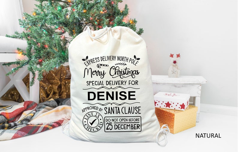 May include: A white canvas Christmas gift bag with black text that reads "Express Delivery North Pole Merry Christmas Special Delivery For Denise Approved By: Santa Clause List 2X Checked Do Not Open Before 25 December".