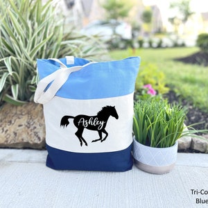 May include: A blue, white, and navy blue tote bag with a silhouette of a horse and the name "Ashley" printed on the front.