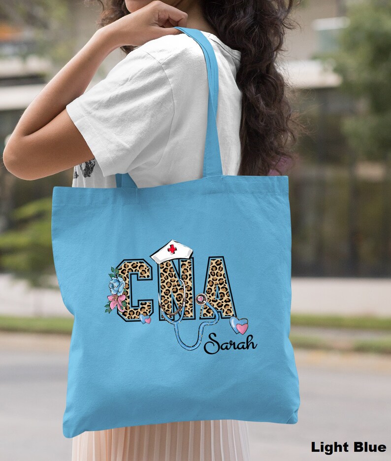 May include: Light blue tote bag with a leopard print "CNA" design, a stethoscope, a red cross, and flowers. The name "Sarah" is written below the design.