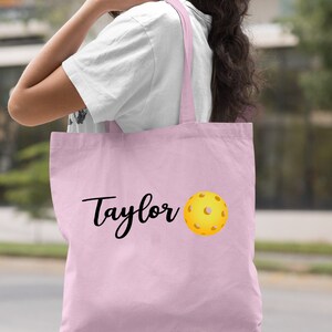K&ouml;nnte beinhalten: Hellrosa farbene Einkaufstasche mit dem Namen "Taylor" und einem aufgedruckten gelben Pickleball.