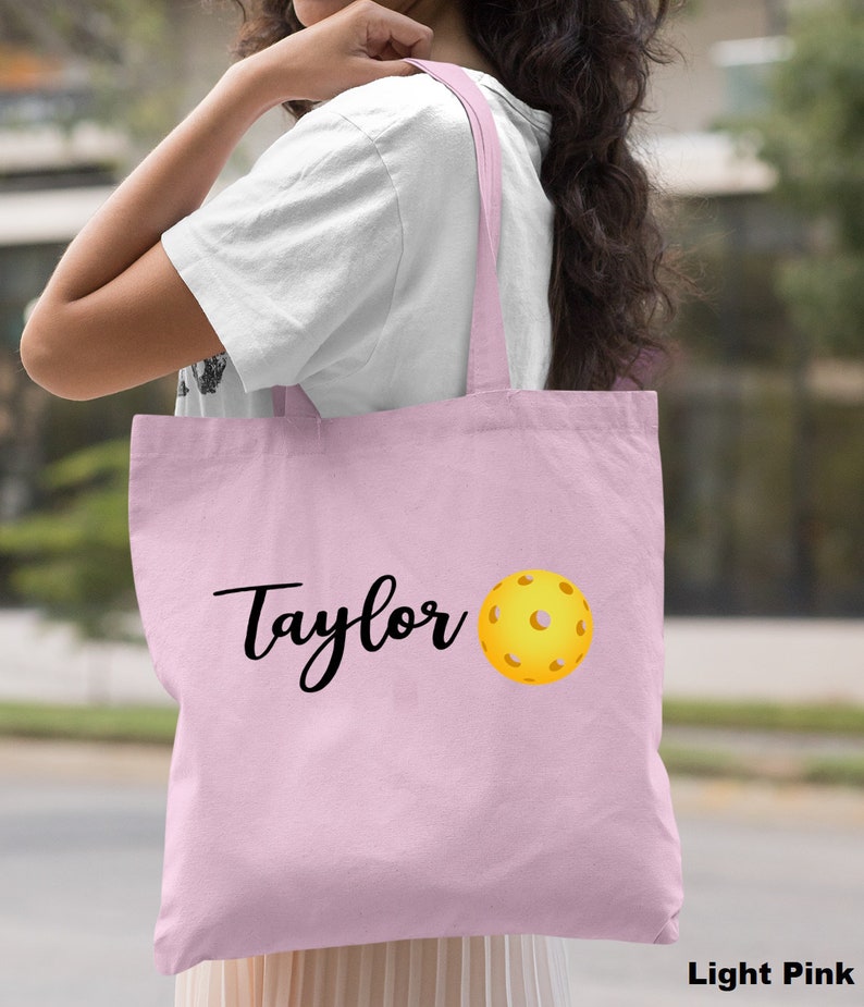 K&ouml;nnte beinhalten: Hellrosa farbene Einkaufstasche mit dem Namen "Taylor" und einem aufgedruckten gelben Pickleball.