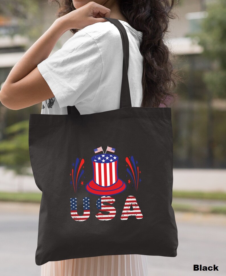 May include: Black tote bag with a red, white, and blue graphic of a top hat with fireworks and the word "USA" in distressed lettering.