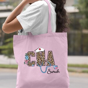May include: Light pink tote bag with a leopard print design that says "CNA" with a stethoscope and a nurse's hat. The name "Sarah" is written below the design.